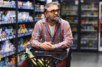 a senior man pushes a cart down a grocery aisle.
