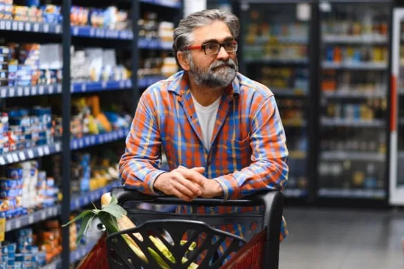 a senior man pushes a cart down a grocery aisle.
