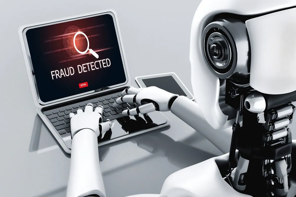 a robot is typing on a laptop while the screen says fraud detected.