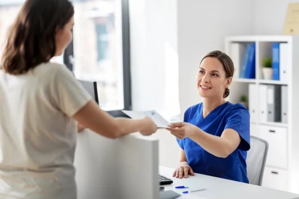 a medical worker hands a document to an office receptionist.