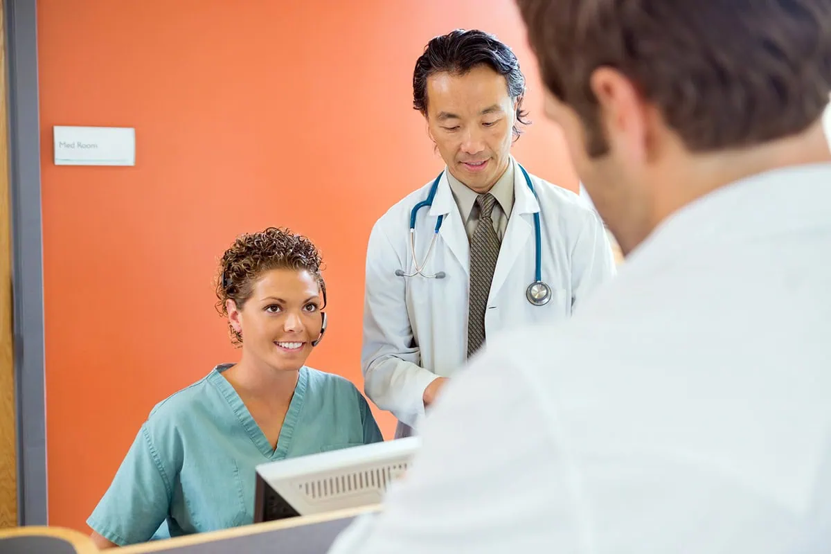 a nurse receptionist and a doctor in an office with a very orange wall.