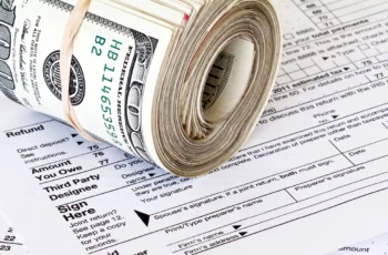 a roll of hundred dollar bills sits on a tax return.