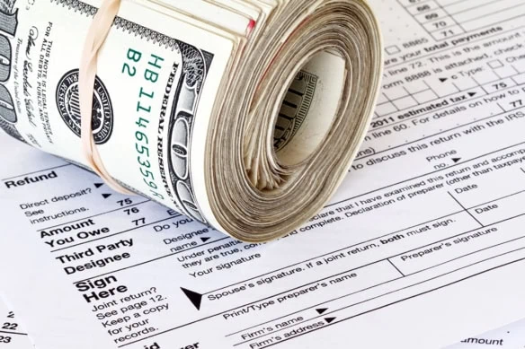 a roll of hundred dollar bills sits on a tax return.