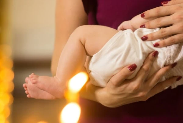 baby legs on the hands of godparents in the cathedral against the background of candles and altar