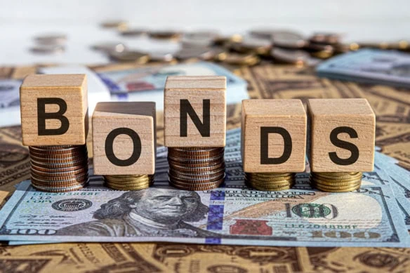 wooden blocks spelling bonds laid atop coins and cash.