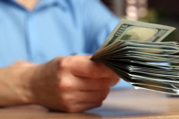 a person holds out a stack of hundred dollar bills.