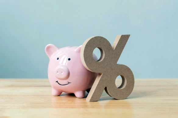 a piggy bank sits next to a wood block percent sign.