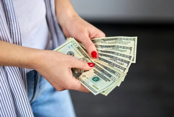 a woman with painted nails fans out numerous 20 dollar bills.