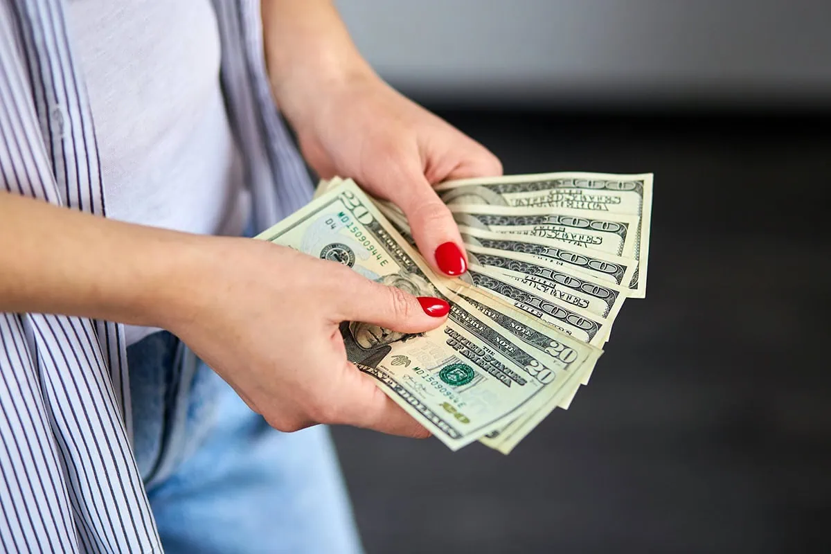 Boost Your Income: 10 Best Dividend Funds for 2026 2 a woman with painted nails fans out numerous 20 dollar bills.