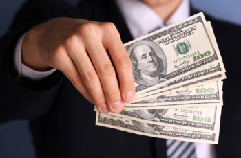 a businessman holds several hundred dollar bills in front of him.