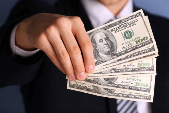 a businessman holds several hundred dollar bills in front of him.