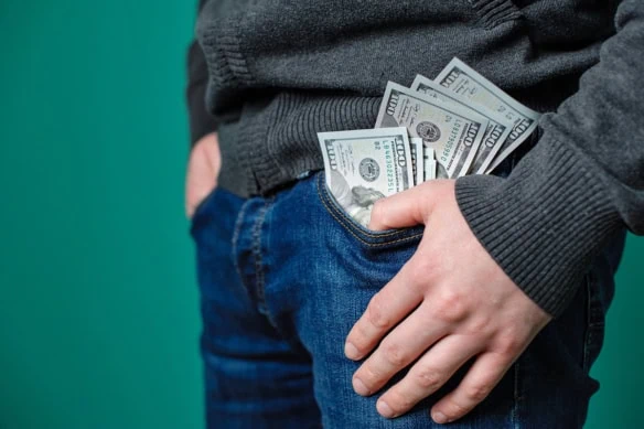 a man wearing jeans has many hundred dollar bills spilling out of his pants.