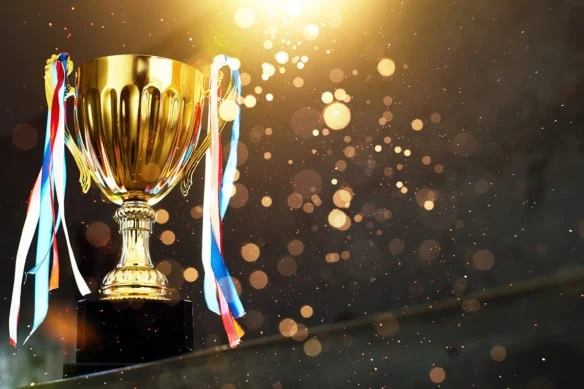 a golden trophy with ribbons against a dark background with shining gold light spots.