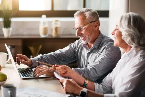 a senior man and woman smile while studying something on their laptop.
