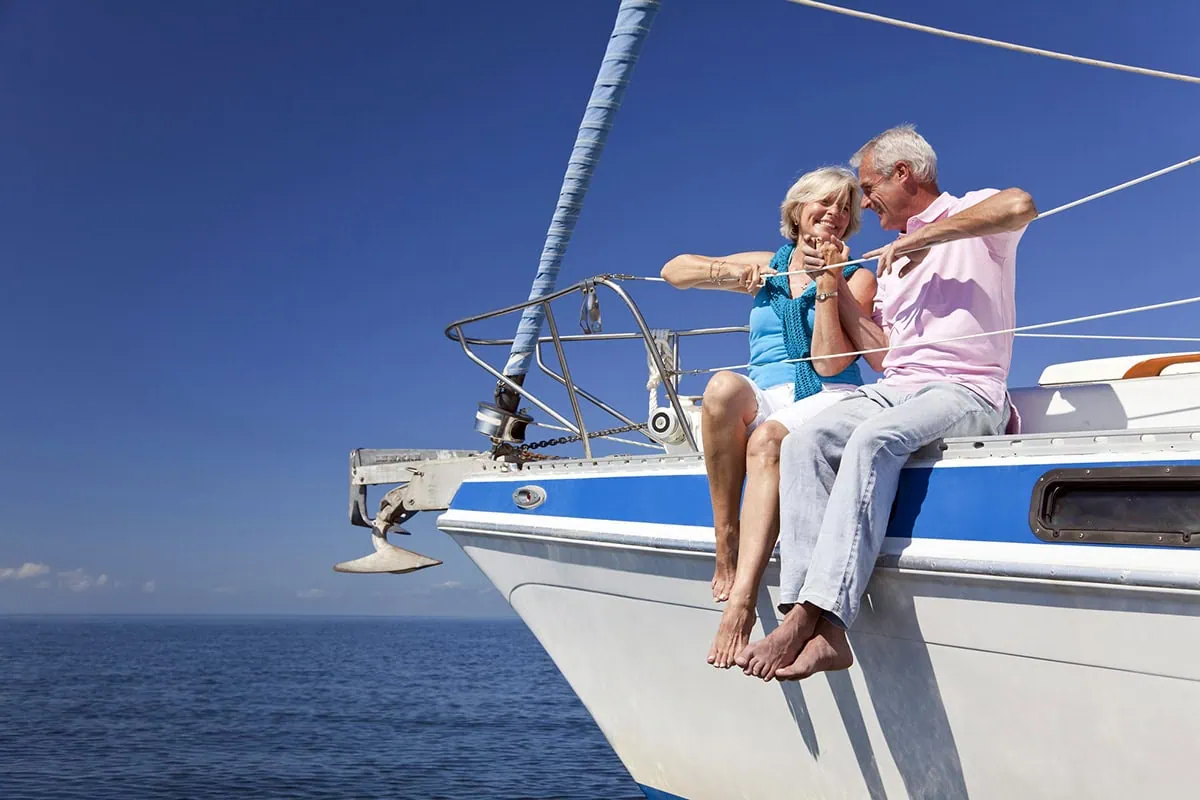 Retiring Early? Avoid These 10 Common Mistakes 6 an older couple sits on the edge of a boat smiling at one another.