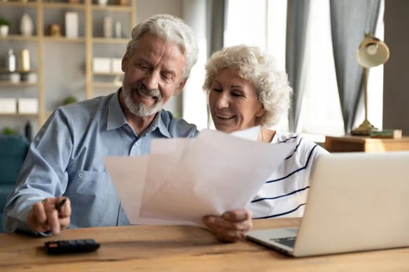 a couple looks at their bills with a laptop nearby.