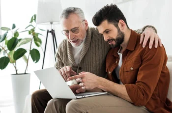 an older father and son look at something on a laptop.