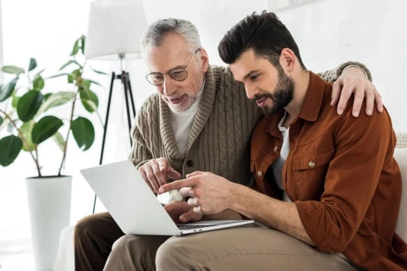 an older father and son look at something on a laptop.