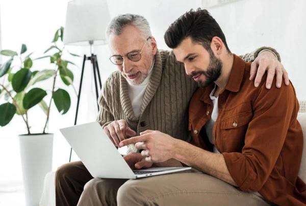 an older father and son look at something on a laptop.