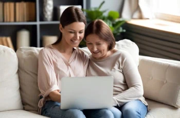 a happy adult daughter and mother use a laptop together.
