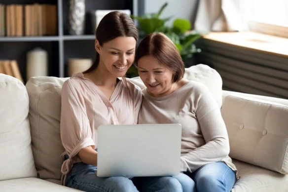 a happy adult daughter and mother use a laptop together.