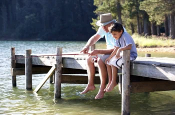 a grandfather and his grandson are fishing off a lake pier.