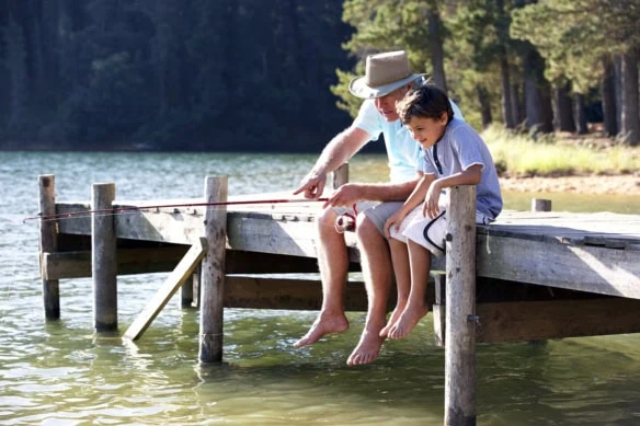 a grandfather and his grandson are fishing off a lake pier.