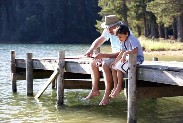 a grandfather and his grandson are fishing off a lake pier.