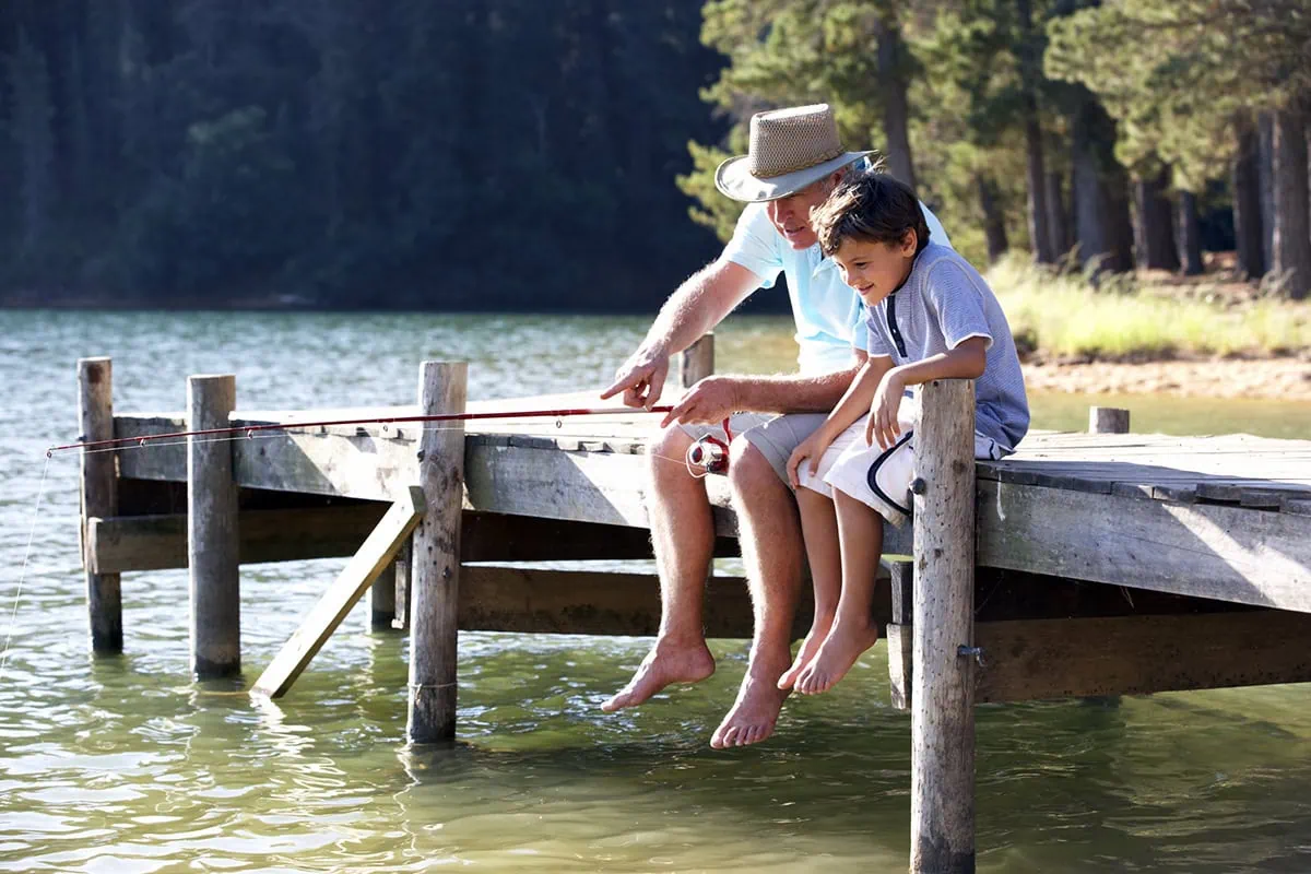 Calming the Golden Years: 10 Practical Strategies to Silence Retirement Anxiety 2 a grandfather and his grandson are fishing off a lake pier.