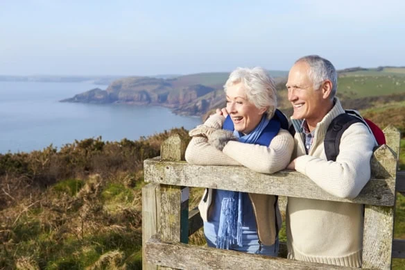 a senior couple stands on a wooden perch and looks at the coastline during the fall season.