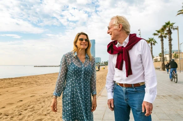 a happy senior couple walks seaside in barcelona.