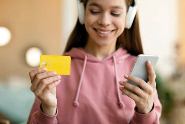 A girl in headphones looks at a smartphone and a debit card. 1200