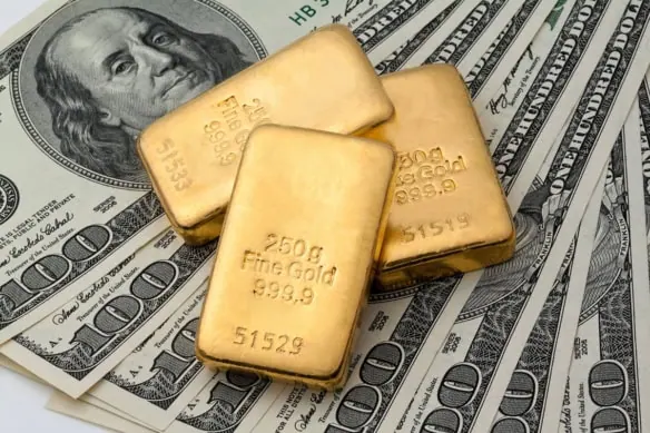 gold bars sit on top of several hundred dollar bills.