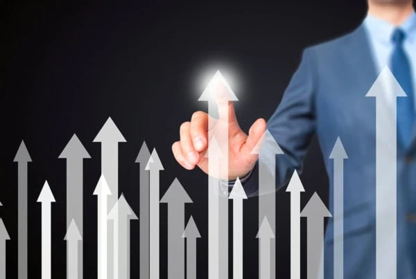 a businessman points to one of several white arrows pointing upward.