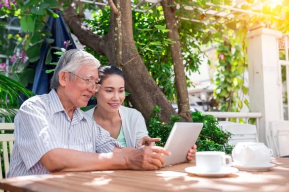 an older asian man and his middle aged daughter look at a laptop.