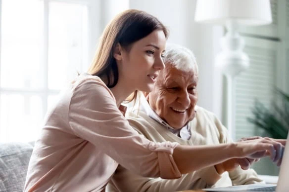 an old person and a young person look at a laptop.
