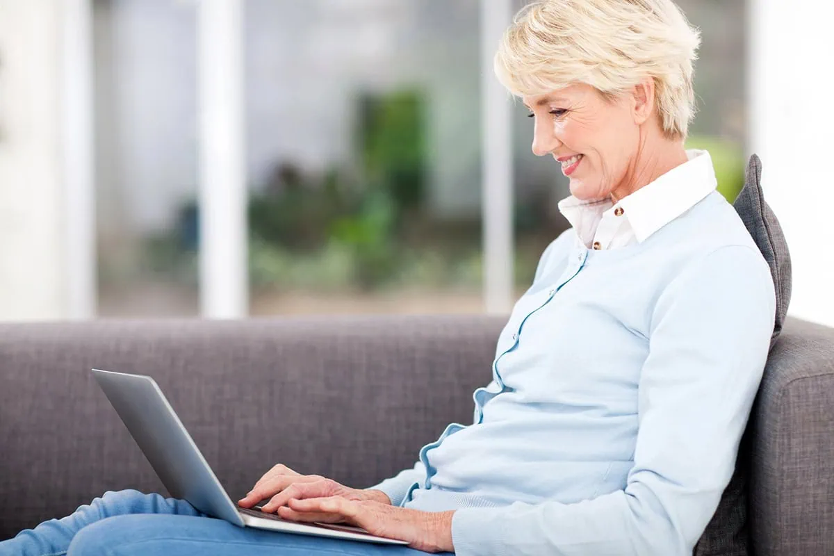 a happy senior woman typing on a laptop.