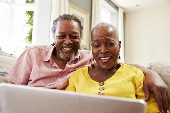 a smiling senior couple use their laptop while sitting on a sofa.