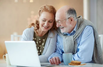 couple looks at a laptop while drinking tea and eating biscuits.