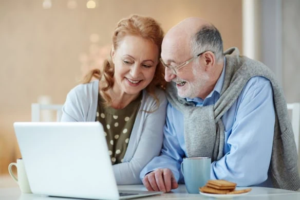 couple looks at a laptop while drinking tea and eating biscuits.