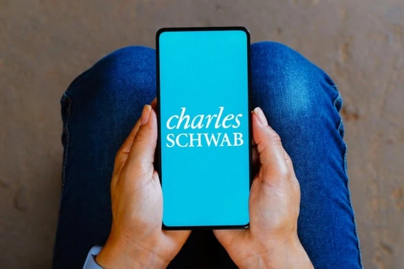 a person stares down at their phone which has a charles schwab logo on the screen.
