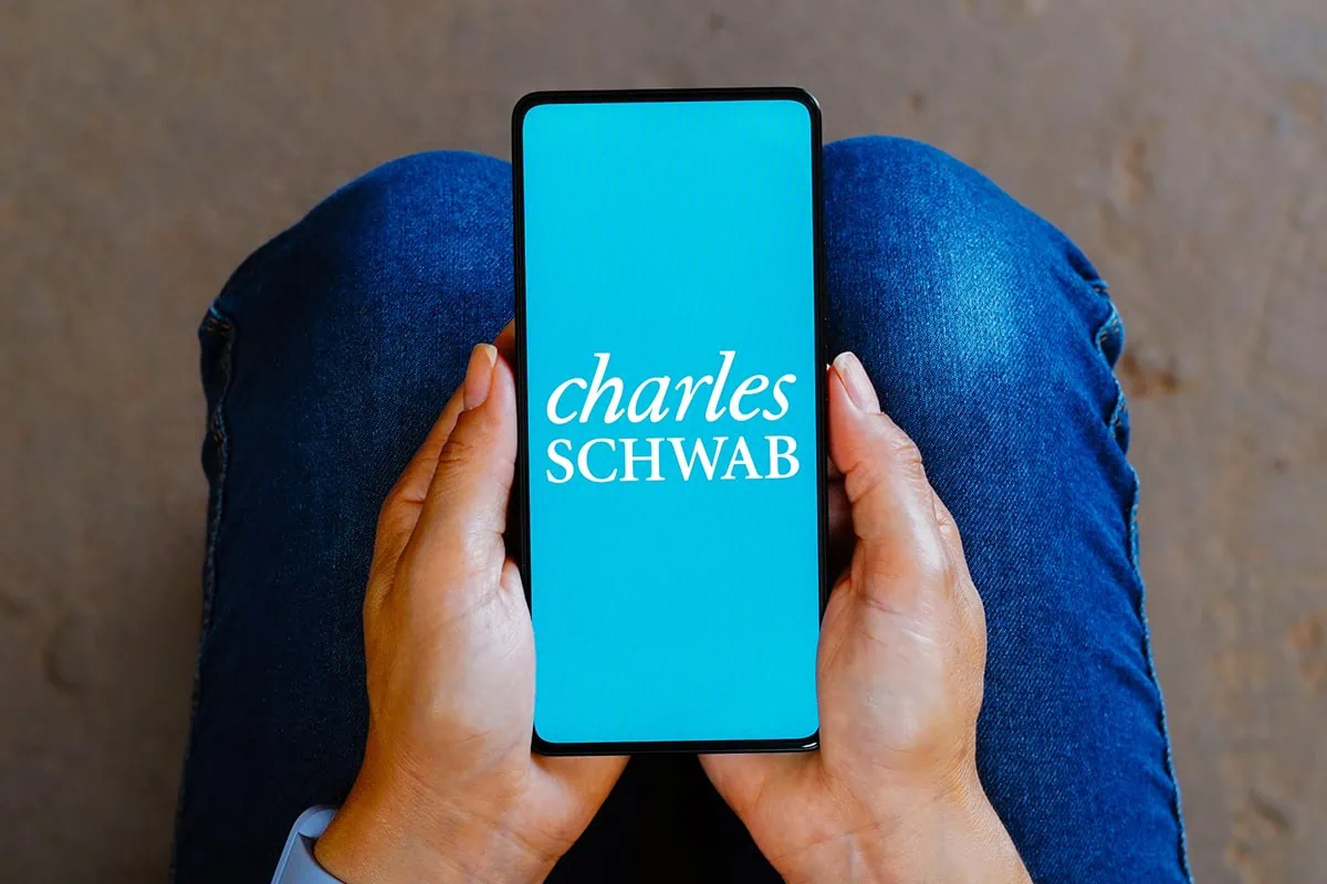 a person stares down at their phone which has a charles schwab logo on the screen.