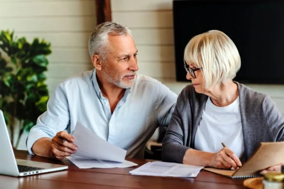 a middle-aged couple fills out documents at their table.