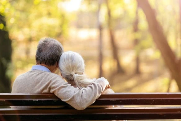 a senior couple cuddles on a park bench.