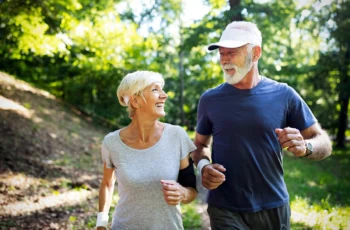 an older couple smiling at each other while jogging in a park.