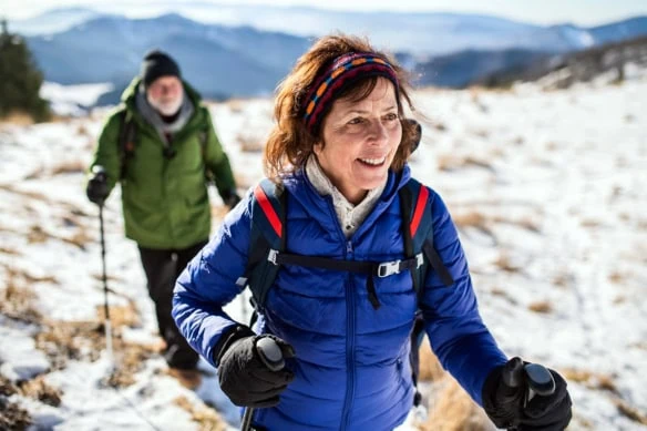 Senior couple with nordic walking poles hiking in snow.