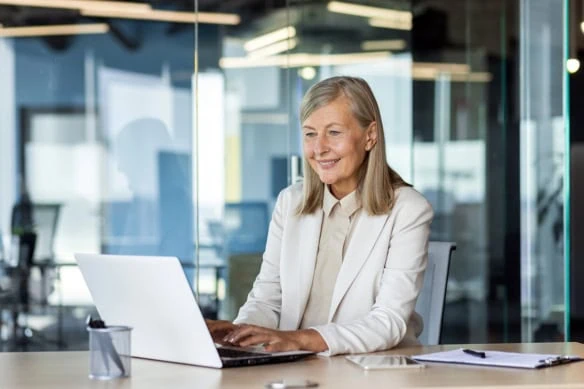 a businesswoman looks at her laptop while working in a glass building.