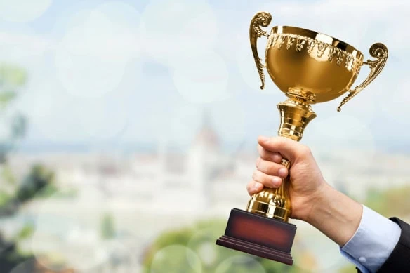 a hand holds a trophy against a blurred background of a city.