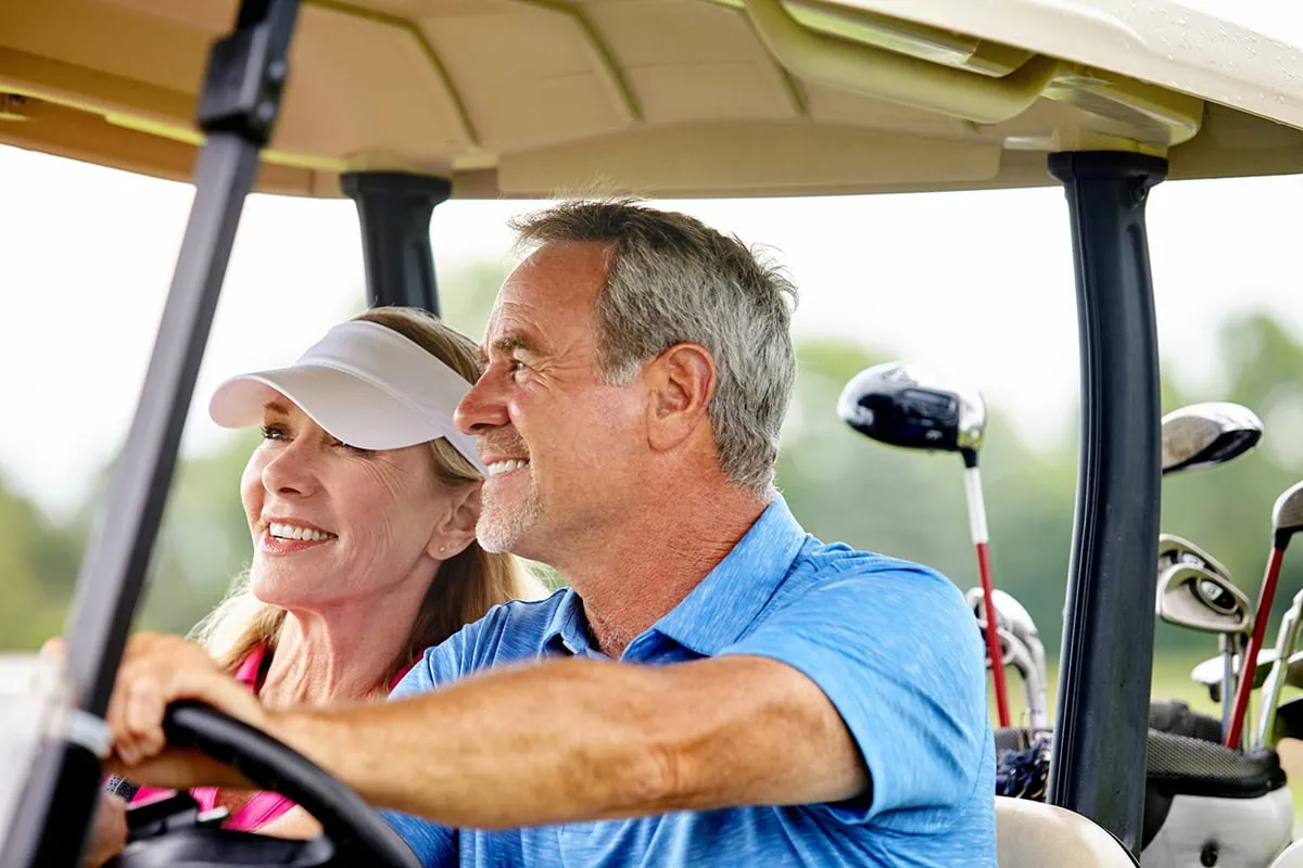 When Pre-Owned Is Preferred: Never Buy These 10 Items New 2 a retired man and woman smile while driving a golf cart.