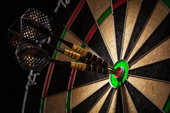 a light shines on three darts sitting in the bullseye of a dartboard.